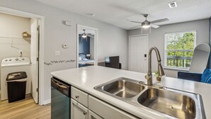 Une cuisine de taille réduite dotée d’un îlot central, d’un évier en acier inoxydable et d’un ventilateur de plafond.