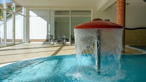 En pool med vandelement, opholdsområde med siddepladser indendørs og store vinduer.