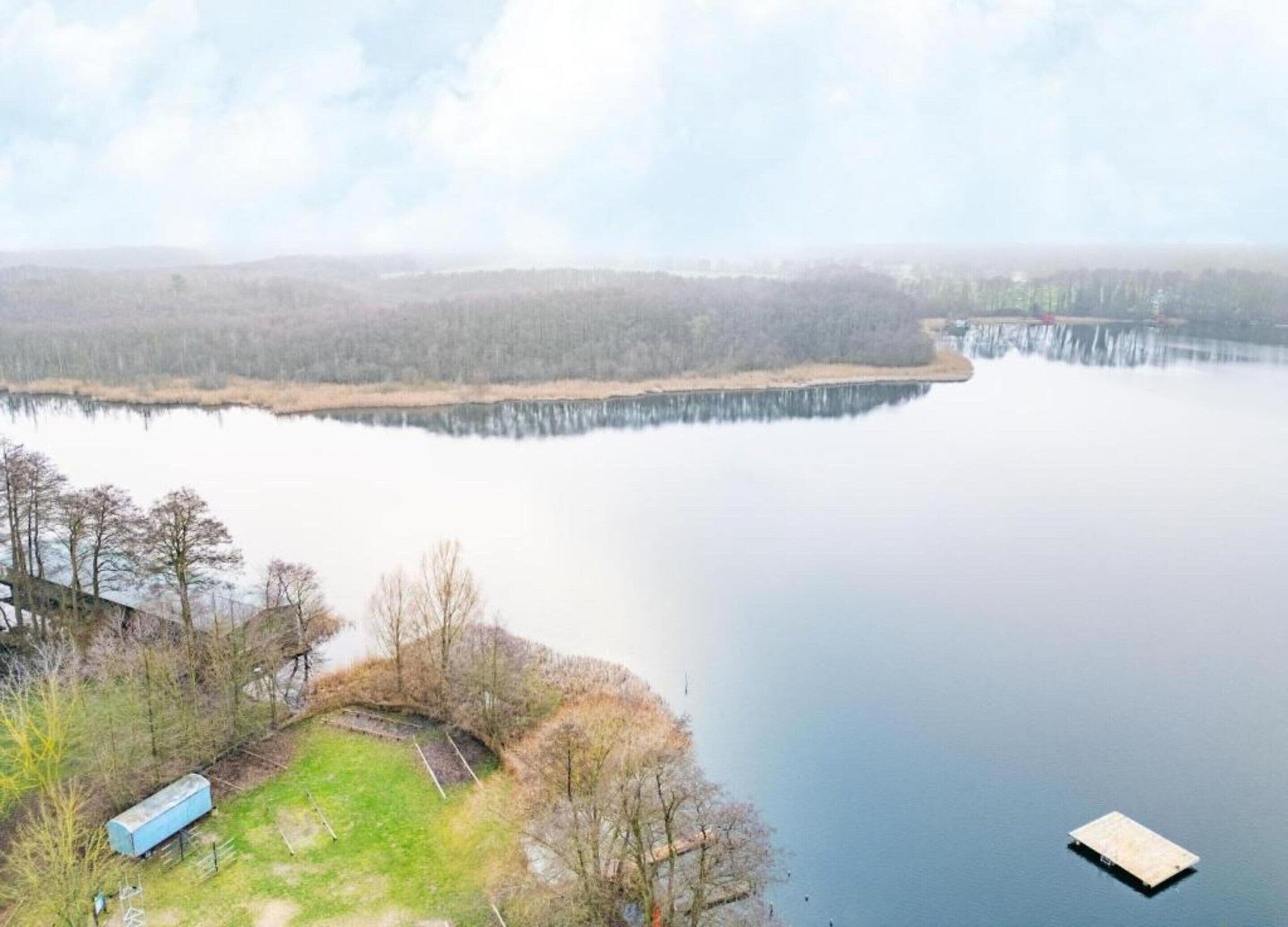 A calm lake with a dock and a small building on the shore.