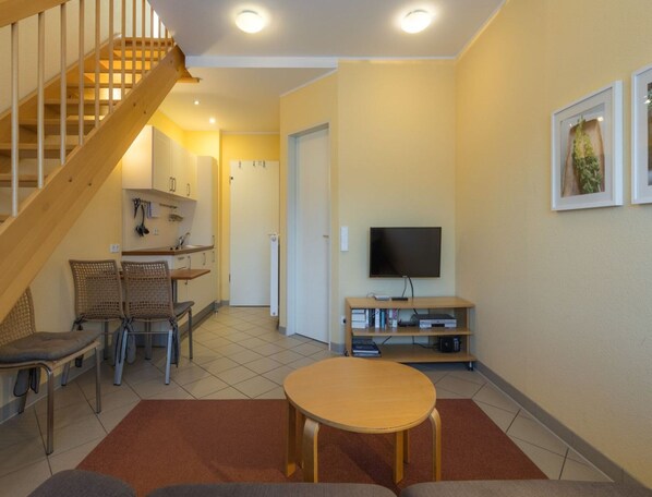 A living room with a wooden staircase, a TV, a dining area with chairs, and a kitchen in the background. - Unvergessliches Apartment am See (Mirow)