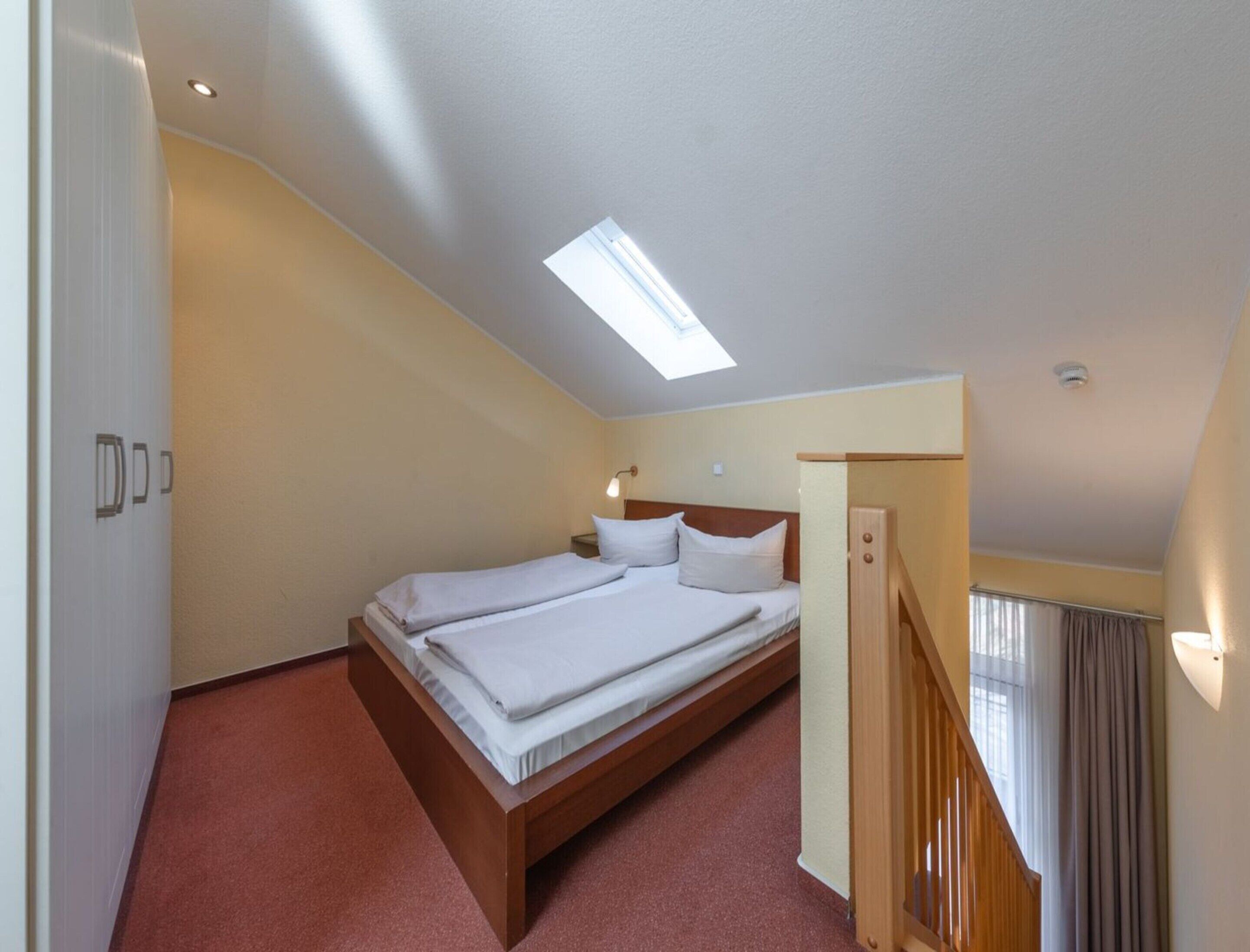 Ein Schlafzimmer mit Bett, Oberlicht, einer Holztreppe und einer Tür mit Griff.