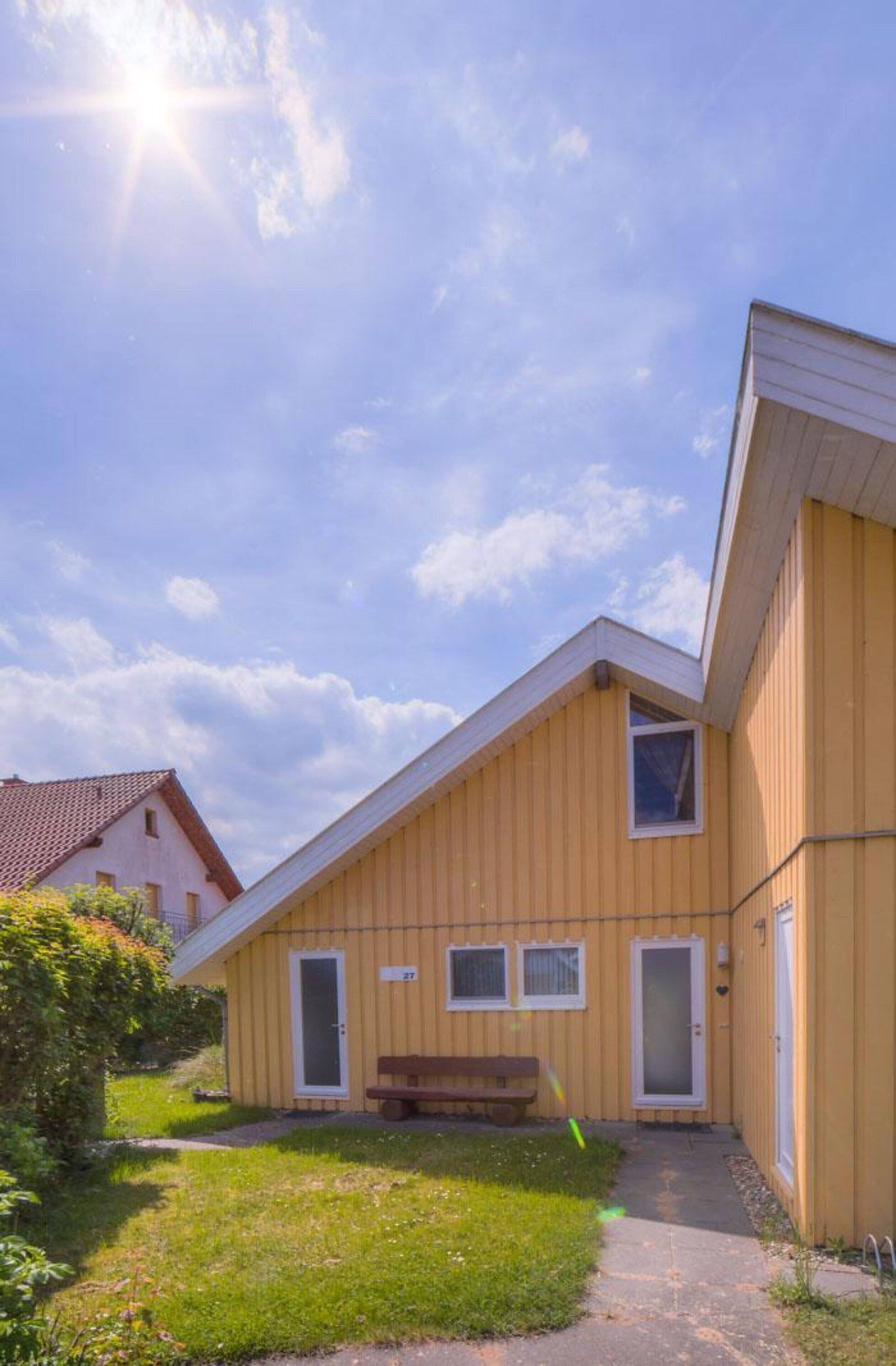 A yellow building with a sloped roof, a bench, and a pathway leading to the entrance.