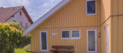 A yellow building with a sloped roof, a bench, and a pathway leading to the entrance.