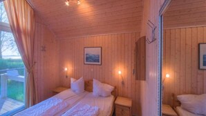 Une chambre dans une cabane en bois, avec un lit, deux tables de chevet et une fenêtre avec des rideaux.