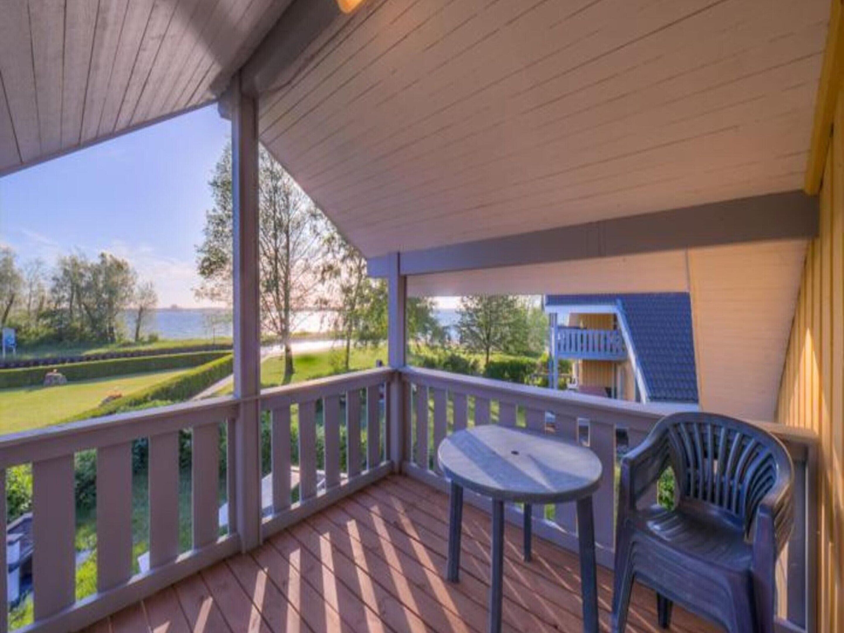 A covered outdoor area with a wooden deck, a small round table, and a plastic chair.