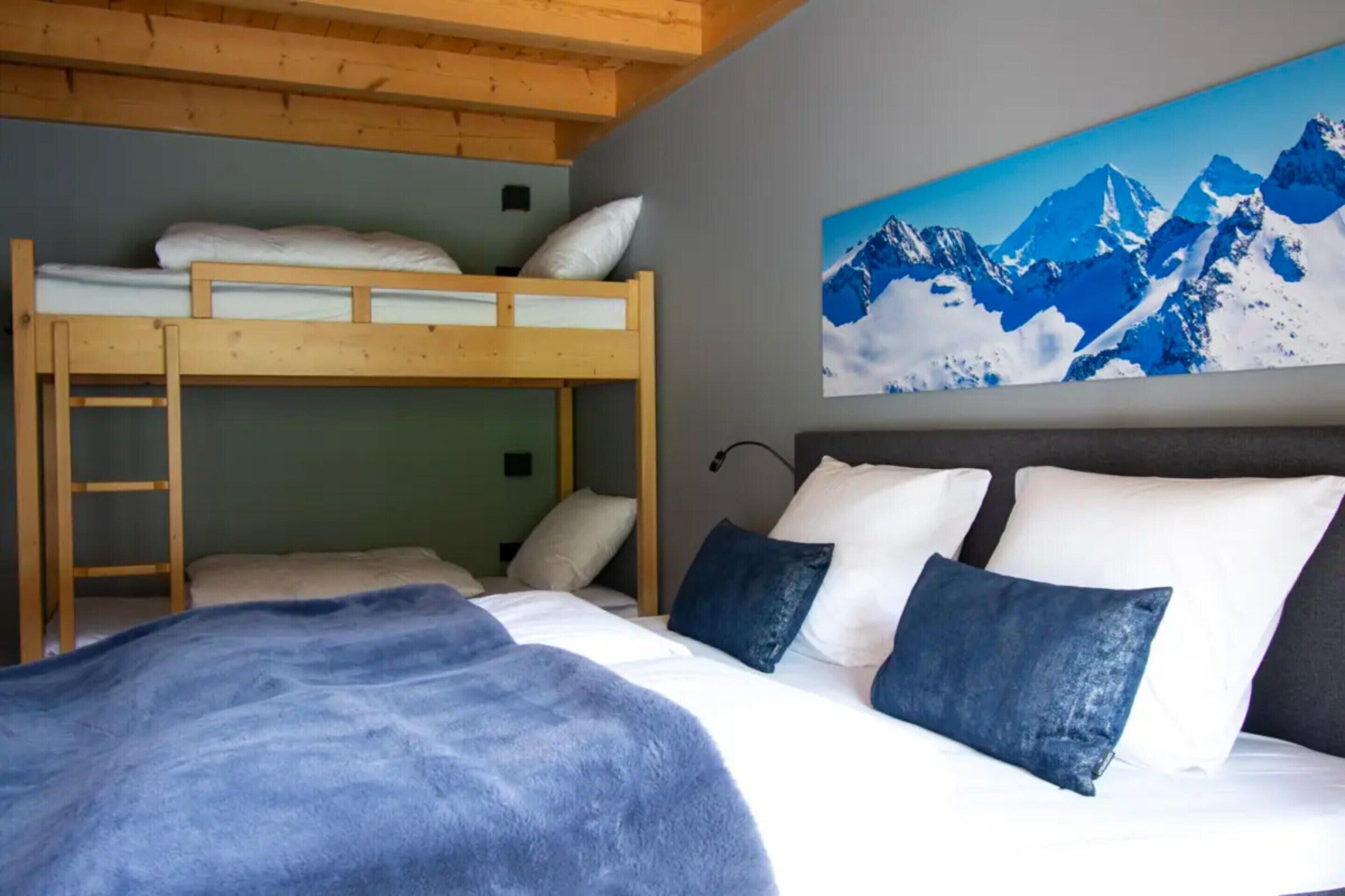 Una habitación con literas, la litera inferior con una escalera, una cama grande con almohadas y un cuadro de montañas.