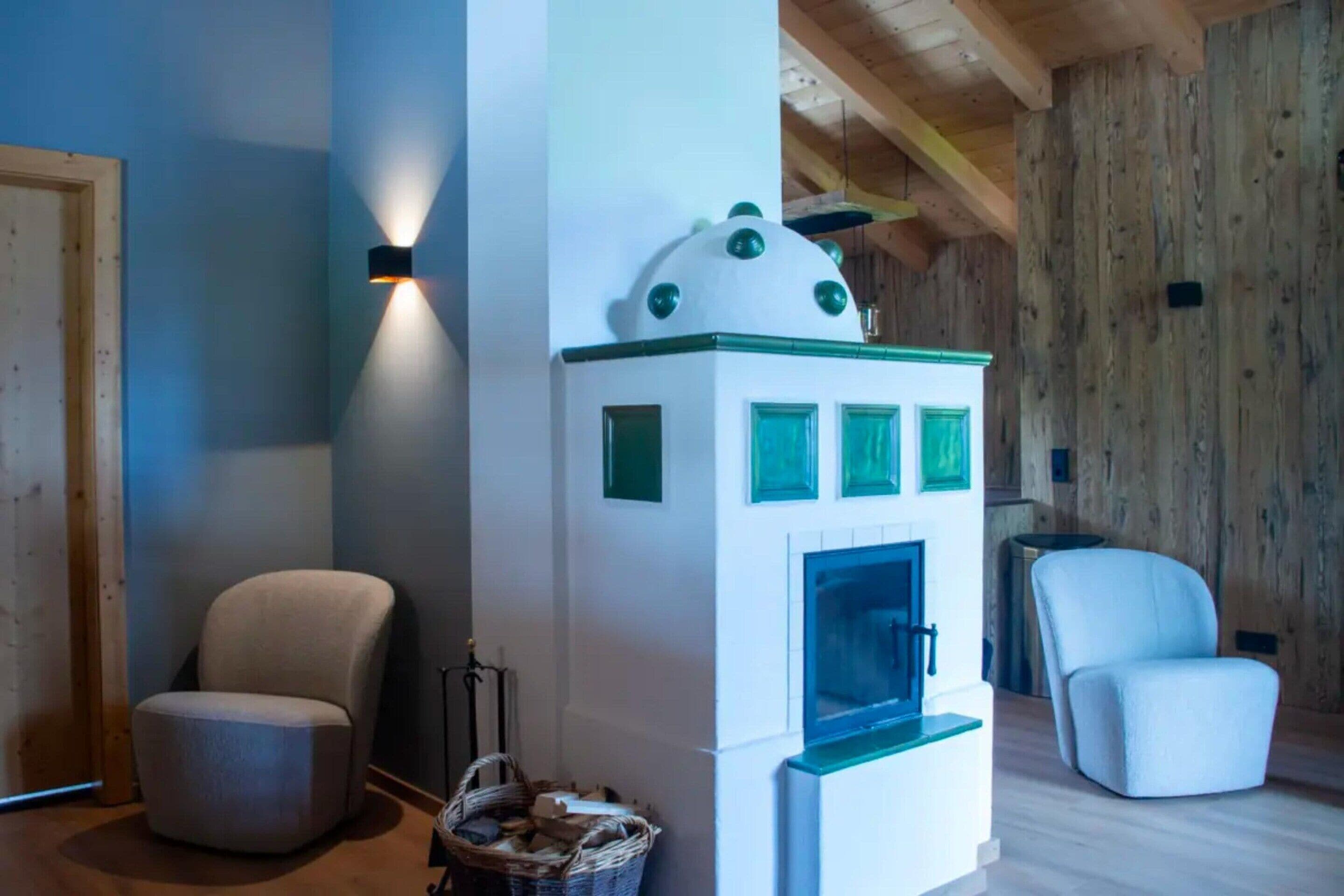 A cozy room with a modern fireplace, two chairs, and a wooden ceiling.