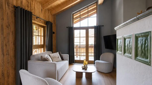A modern living room with a wooden ceiling, a sofa set, a coffee table, and a TV mounted on the wall.
