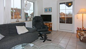 A living room with a grey sofa, a black chair, a glass coffee table, a TV, and a lamp. - Ferienwohnung Petersdorf in Fehmarn-petersdorf (Fehmarn)