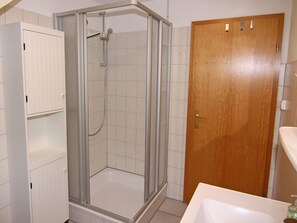 Un baño con ducha compartimentada por vidrio, puerta de madera y lavamanos blanco.