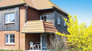 A two-story house with a brick exterior, a tiled roof, and a small porch with a table and chairs. - Ferienwohnung Petersdorf in Fehmarn-petersdorf (Fehmarn)