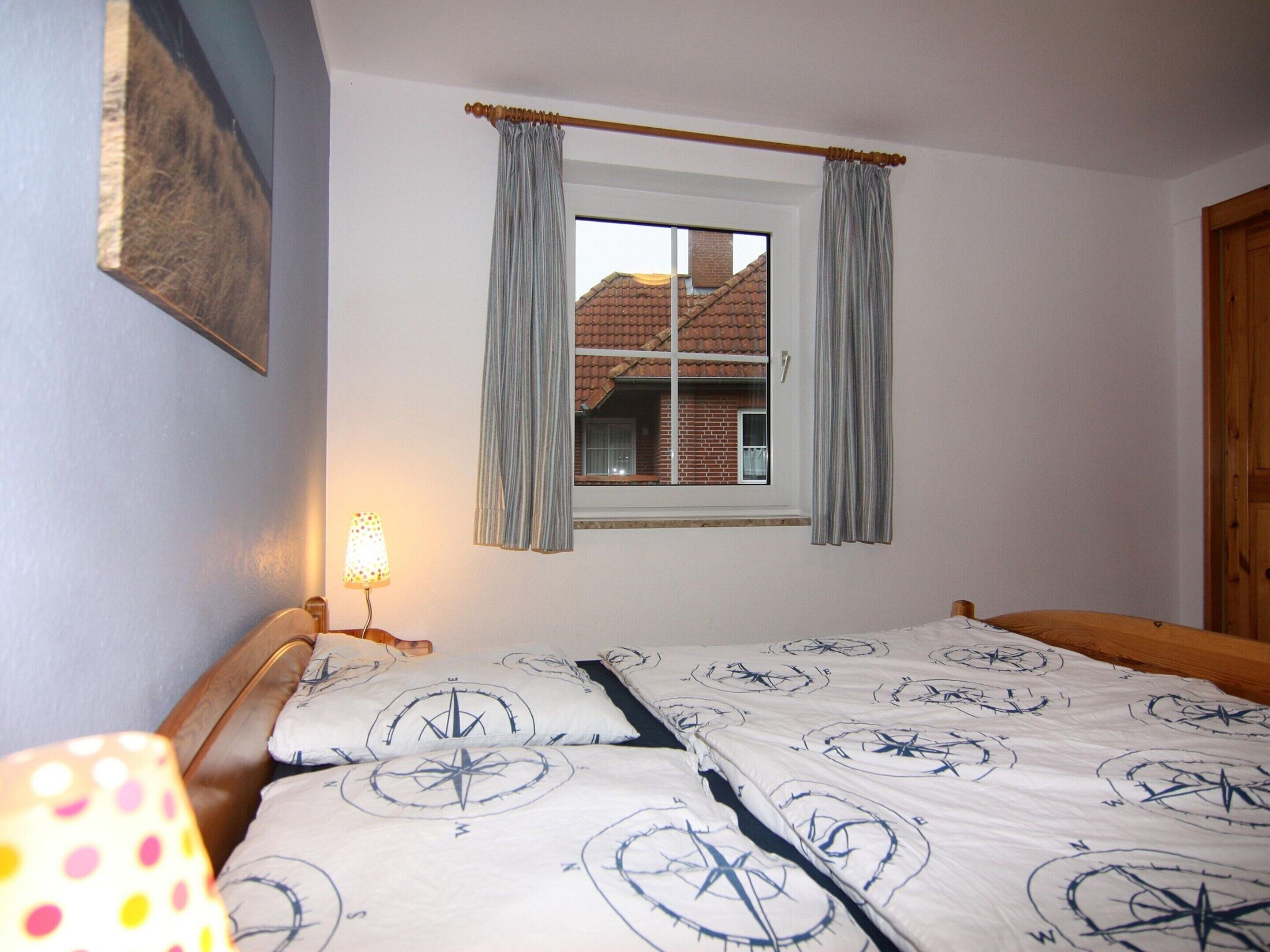 A bedroom with a bed, a window with curtains, a lamp, and a view of a building outside.
