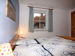 Un dormitorio con cama, ventana con cortinas, lámpara y vista a un edificio.