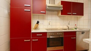 A kitchen with red cabinets, a stainless steel oven, and a dishwasher.