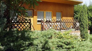 A wooden cabin with a fenced porch, surrounded by dense greenery.