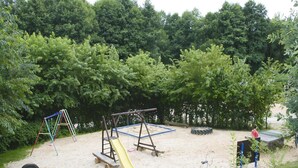 A playground with swings, a slide, and a tire swing set in a sandy area surrounded by trees.