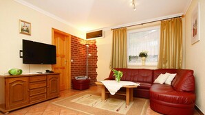 A living room with a red leather sofa, a wooden cabinet, a flat-screen TV, and a brick wall.