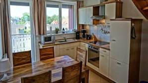 A compact kitchen with a wooden dining table, a microwave, a stove, and a refrigerator. - Liebevoll Eingerichtetes Appartement (Rechlin)