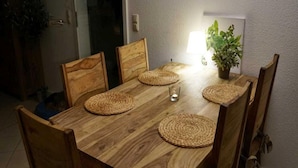 A wooden dining table with woven placemats, six wooden chairs, and a potted plant on the table. - Liebevoll Eingerichtetes Appartement (Rechlin)