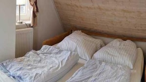 A single bed with white bedding in a room with a sloped ceiling and a brick wall. - Liebevoll Eingerichtetes Appartement (Rechlin)