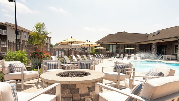 An outdoor pool area with lounge chairs, a fire pit, and umbrellas.