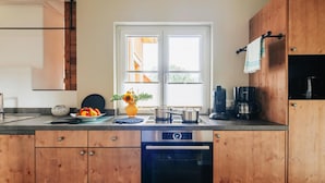 A modern kitchen with wooden cabinets, a dishwasher, a sink with a kettle, and a window with blinds. - Doppelhaushalften mit Kamin in Torfhaus, Harz (Clausthal-Zellerfeld)