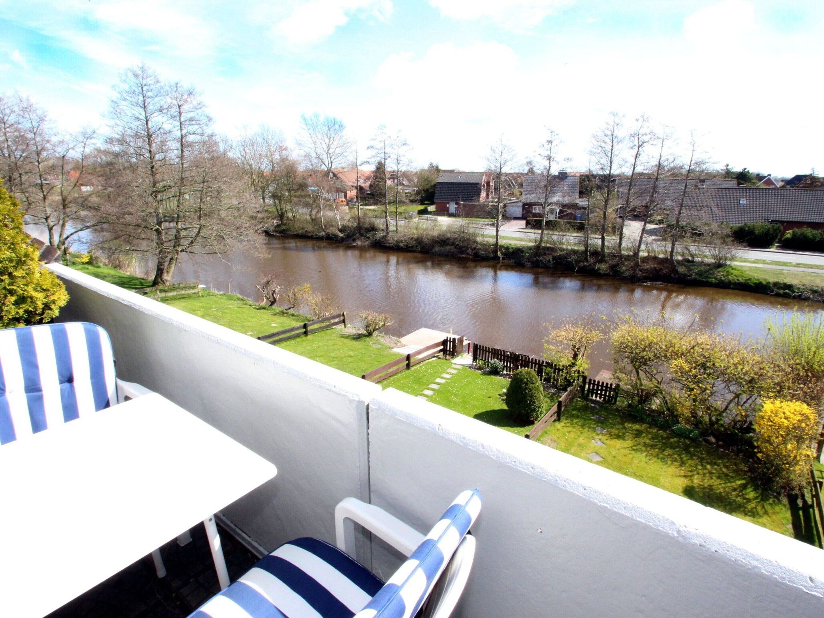 Ein Balkon mit Blick auf einen Fluss, eine Rasenfläche und einen Zaun.