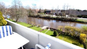 Un balcon donnant sur une rivière, une pelouse et une clôture.