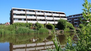 Un immeuble résidentiel à plusieurs étages, doté d’une architecture moderne, situé au bord d’un plan d’eau dont les eaux reflètent la lumière.