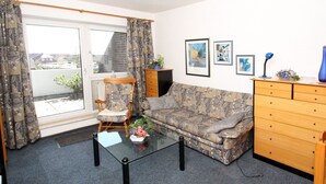 Un salon avec un canapé à motifs, une chaise en bois, une table basse en verre et une commode en bois.