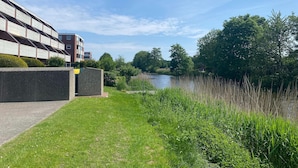 Une vue sur la rivière, avec un bâtiment moderne, des espaces verts et de nombreux arbres.