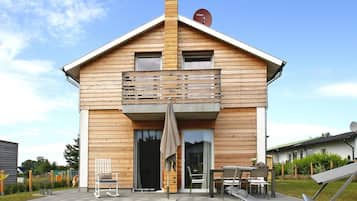 A two-story wooden house with a balcony, a sliding glass door, and a patio with outdoor furniture.