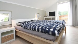 Ein modernes Schlafzimmer mit einem hölzernen Bett, einem Nachttisch mit Lampe sowie einem Fernseher auf einem Schrank.