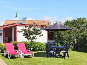 A patio with two red lounge chairs, a table with chairs, and an umbrella. - 6 Person Holiday Home in Falkenberg (Falkenberg)