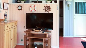 Un salon avec un meuble en bois, un téléviseur posé sur un support en bois et une petite étagère avec des plantes.
