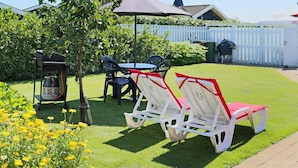 Un jardin avec un barbecue, un coin salon extérieur et une clôture blanche.