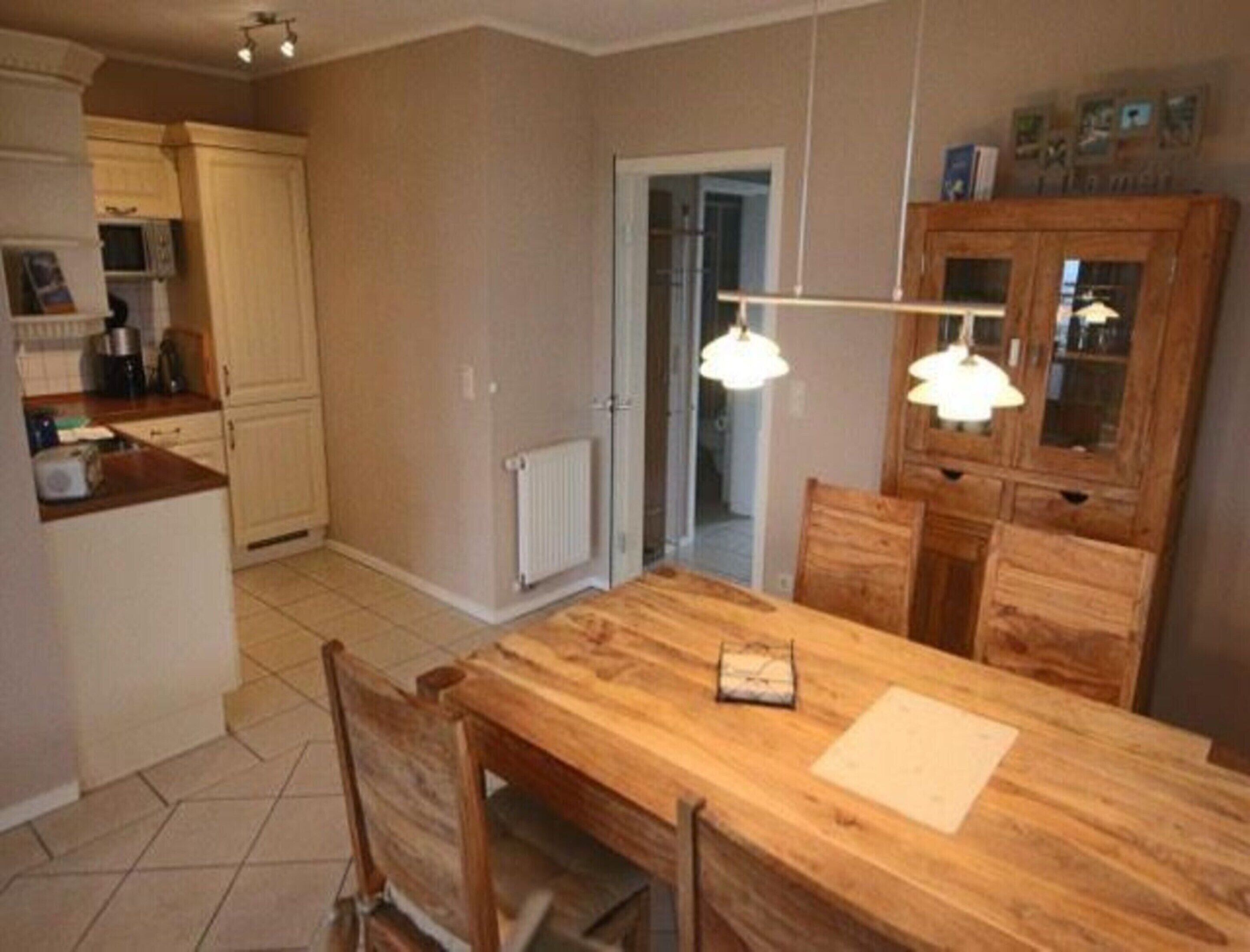 A kitchen with a wooden table and chairs, a white cabinet, and a doorway leading to another room.