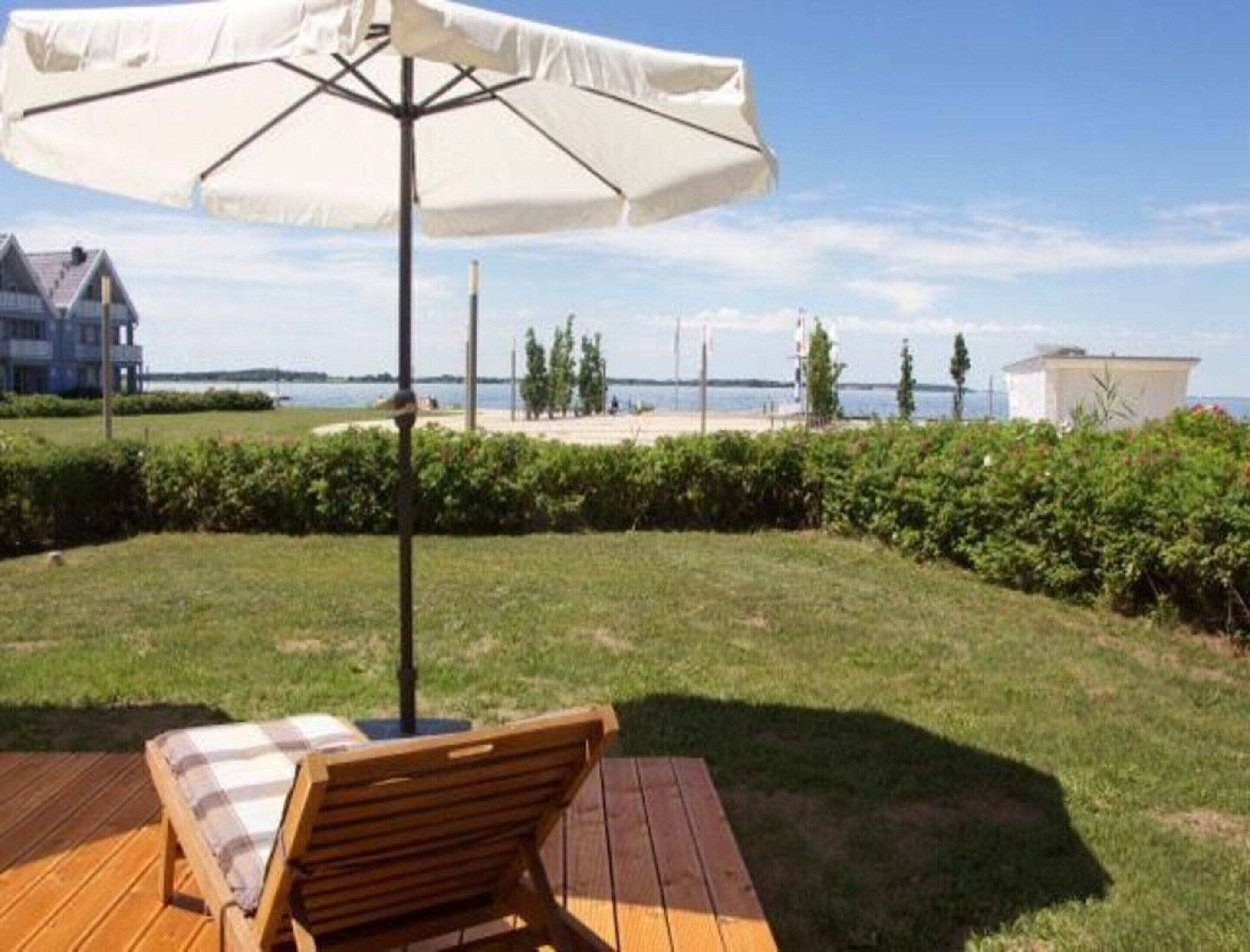 A wooden deck with a single lounge chair and a white umbrella.