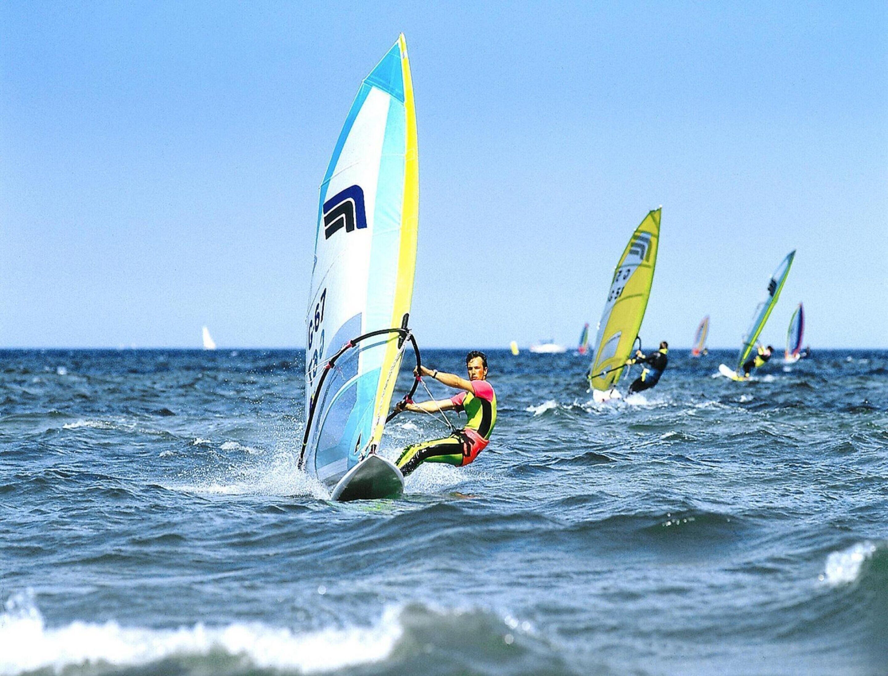 A person windsurfing on the water with multiple sailboards in the background.