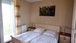 Ein Schlafzimmer mit einem Bett, zwei Nachttischen, einem Fenster mit Vorhängen, einer Heizung und einem Bild an der Wand.