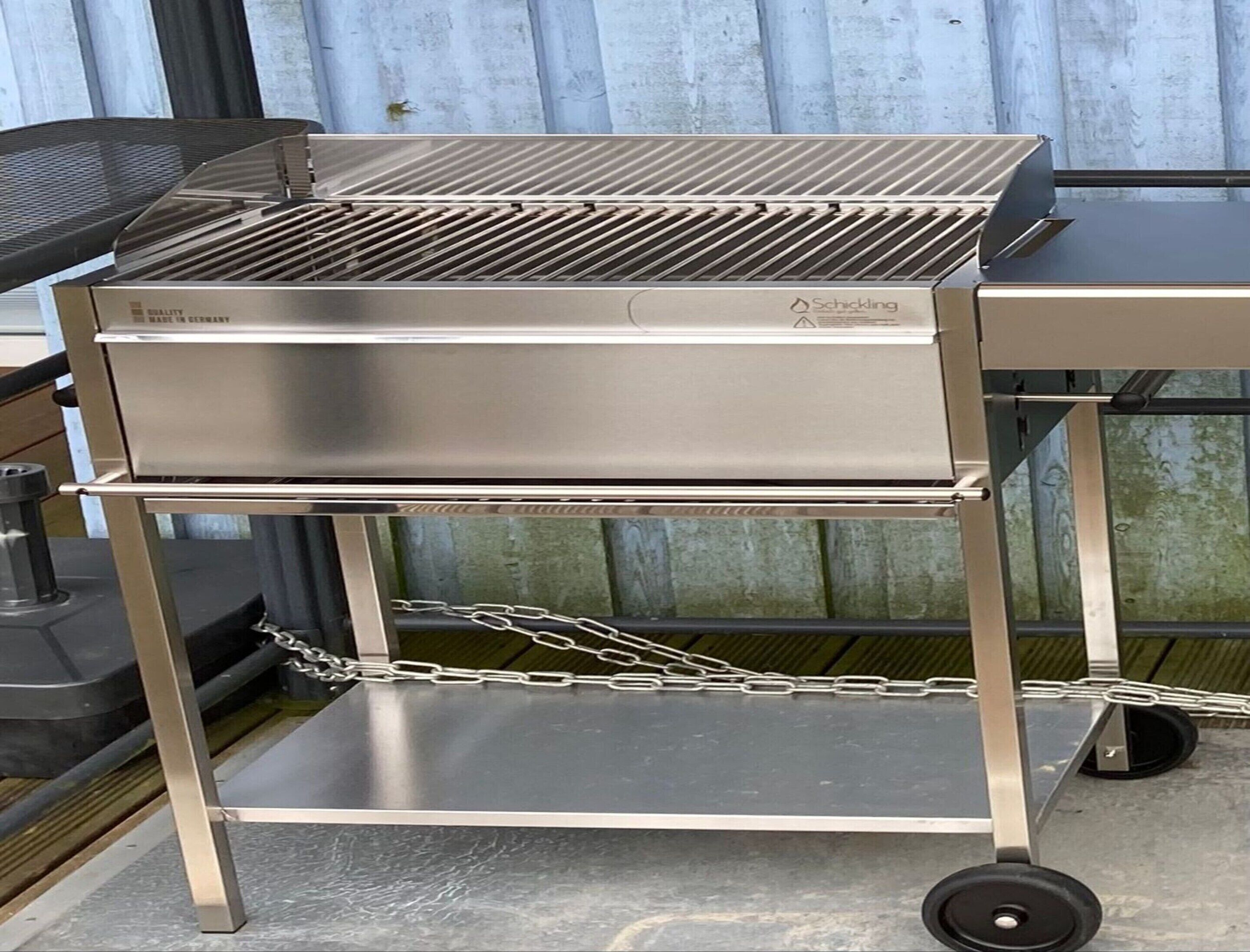 Una parrilla de acero inoxidable con una barrera de cadena, un estante inferior y ruedas.