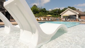 A poolside area with a white lounge chair, a pool, and a building with a yellow umbrella in the background.