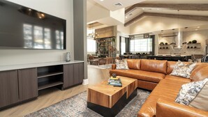 A modern living room with a large flat-screen TV, leather sofa, wooden coffee table, and a patterned rug.