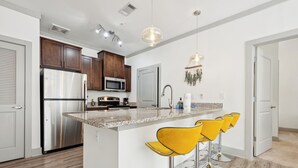 A modern kitchen with stainless steel appliances, a granite countertop, and yellow bar stools. - Overlook 3001 I Modern Apartments in Knoxville (Knoxville)