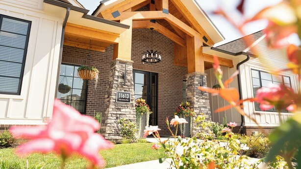 A modern house with a stone facade, a prominent wooden gable, and a well-maintained garden with pink flowers. - Overlook 3001 I Modern Apartments in Knoxville (Knoxville)
