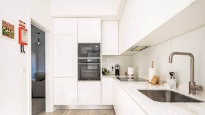 A modern kitchen with white cabinetry, a stainless steel sink, and a built-in oven. - Villa Ana D'Arfet, Água de Pena (Santa Cruz)