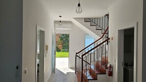 A modern interior with a wooden staircase, a hallway leading to a garden, and a visible fire extinguisher. - Villa Ana D'Arfet, Água de Pena (Santa Cruz)