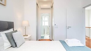 A hotel room with a bed, a nightstand with a lamp, a door leading to a bathroom, and a view of the outside. - Villa Ana D'Arfet, Água de Pena (Santa Cruz)