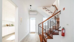 A modern interior with a wooden staircase, white walls, and a kitchen area visible through an open door. - Villa Ana D'Arfet, Água de Pena (Santa Cruz)