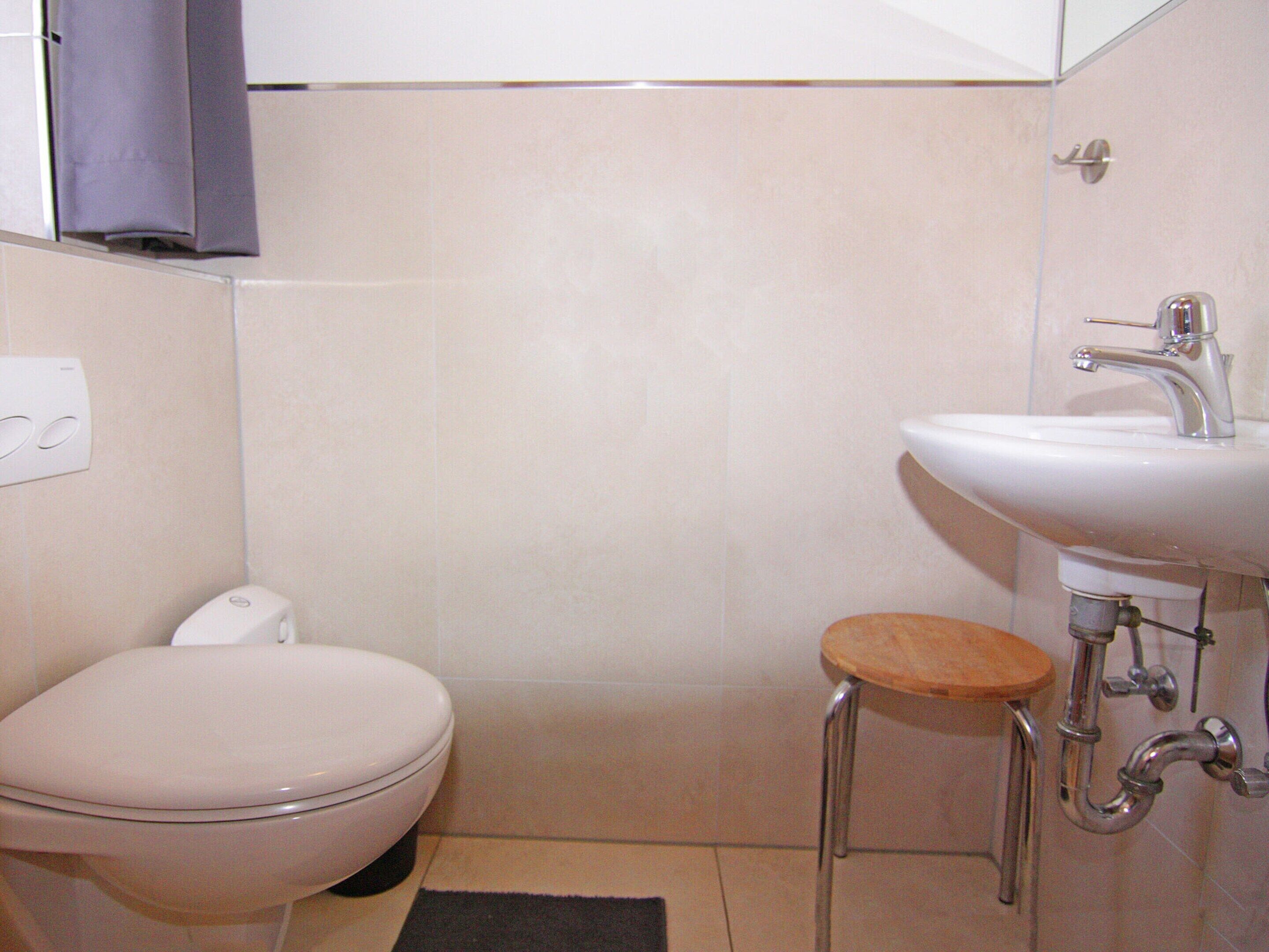 A bathroom with a toilet, sink, and a small stool.